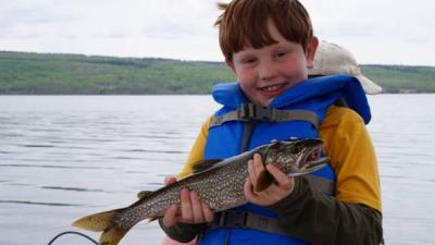 der 8-jährige präsentiert stolz die gefangene Forelle