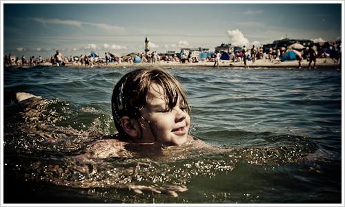 Ein Mädchen schwimmt im Meer, im Hintergrund der Strand mit Menschen Ein Mädchen schwimmt im Meer, im Hintergrund der Strand mit Menschen