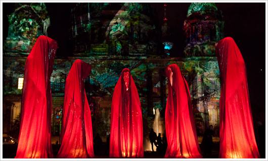 Rote Figuren vor beleuchteter Kirche