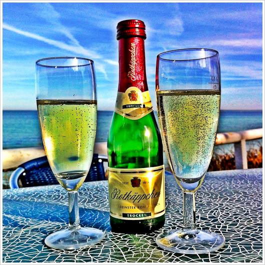 Sektflasche und -glaeser, im Hintergrund Meer